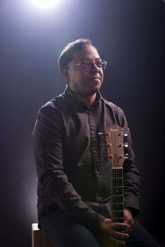 Bijoy Thangaraj standing with an electric guitar under a spotlight