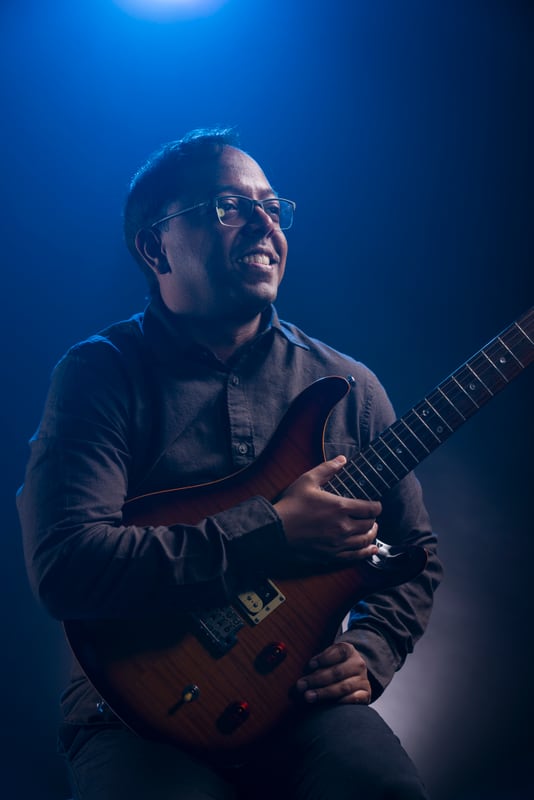 Bijoy Thangaraj holding an electric guitar under blue stage lighting